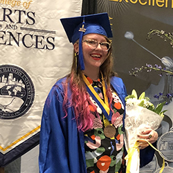 Student wearing a cap and gown holding flowers at graduation.