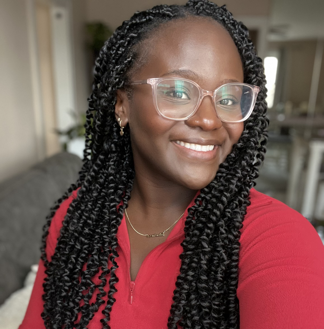 Bahati Kimondo smiling wearing a red sweater in front of a blurred background