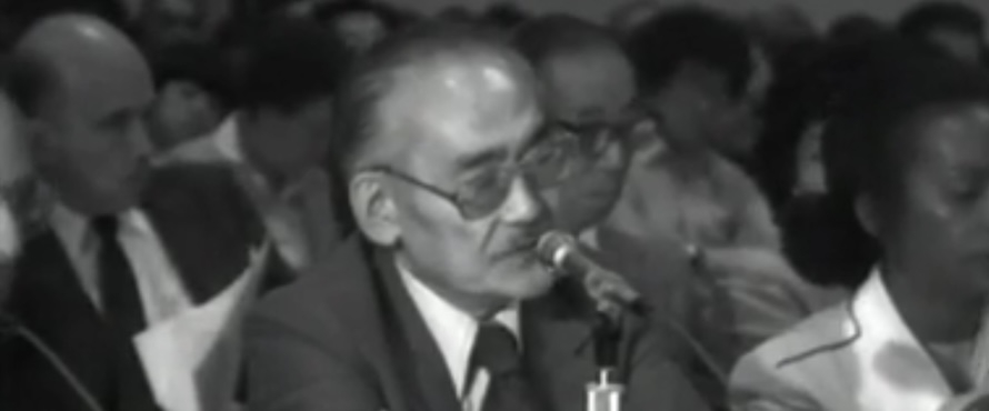 A black and white photo of Minoru Yasui providing testimony during the Commission on the Wartime Relocation and Internment of Civilians hearings held at Northeastern Illinois University in 1981.