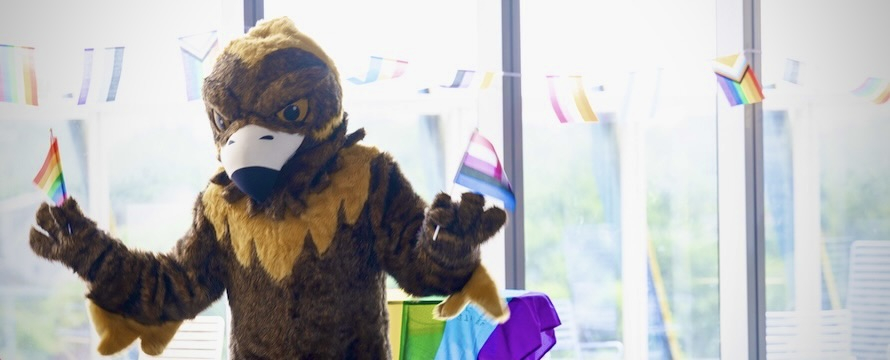 A photo of NEIU's mascot, Goldie, holding PRIDE flags at the University's El Centro location. 