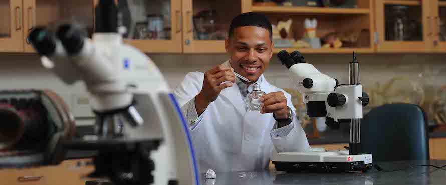 Anthony Smith in a laboratory setting smiling and holding a glass bottle and dropper