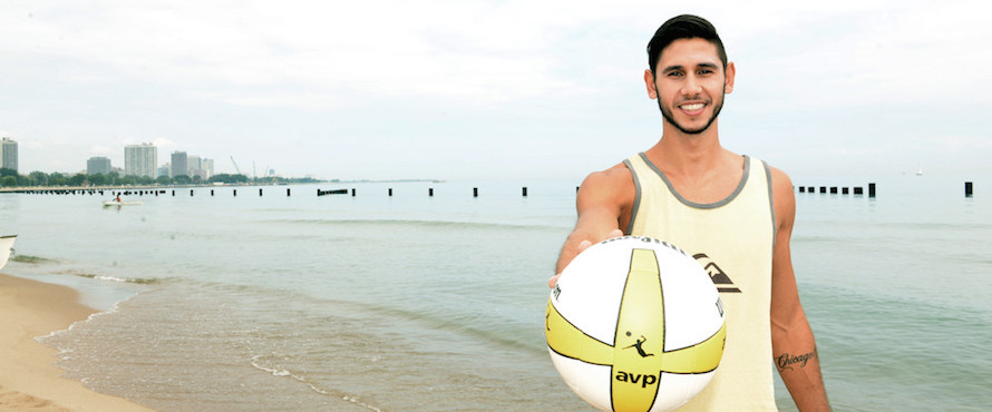 Raffe Paulis holds up an AVP volleyball toward the camera while standing on the beach of Lake Michigan.