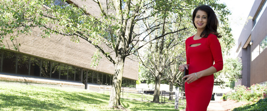 P.J. Randhawa smiles at the camera while standing in front of two trees and a building.