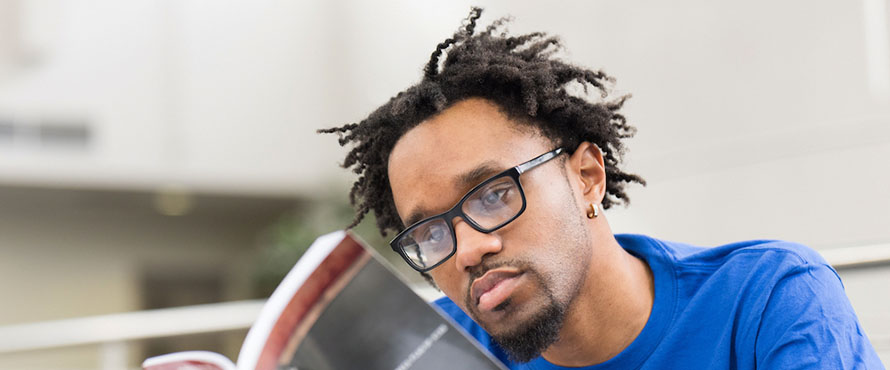 Northeastern student Byron Terry reads a book while wearing a blue Northeastern Illinois University T-shirt.