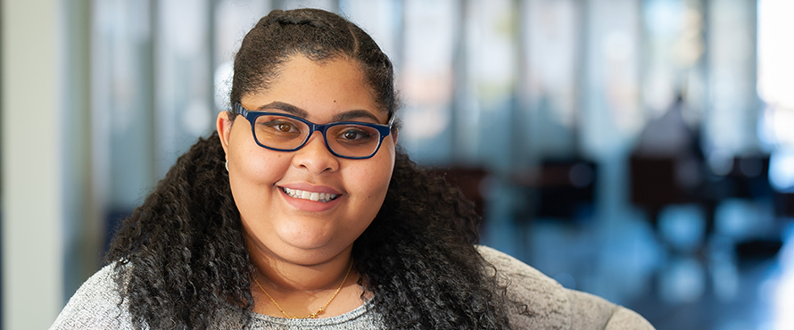 Image of Alecia Martin smiling, wearing a gray shirt and blue rimmed glasses  