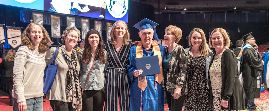 Photo of Bob Dwyer in his blue cap and gown surrounded by his family at Northeastern's May 2019 Commencement.