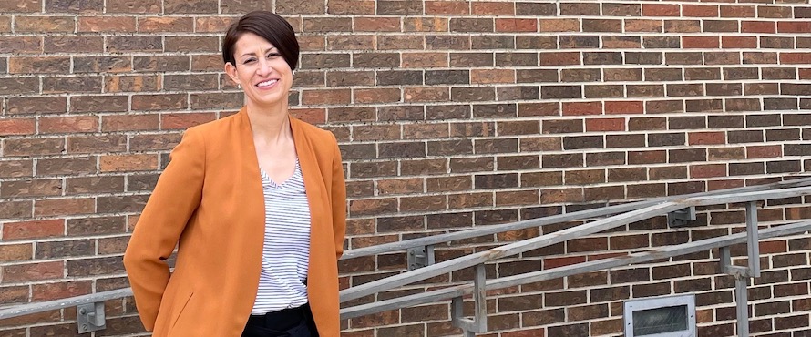 Marisela Palma Barraza in an orange blazer and striped shirt standing near a bring wall