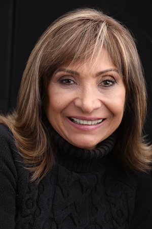 Ana Gil Garcia smiles into the camera while wearing a black sweater in front of a black background.