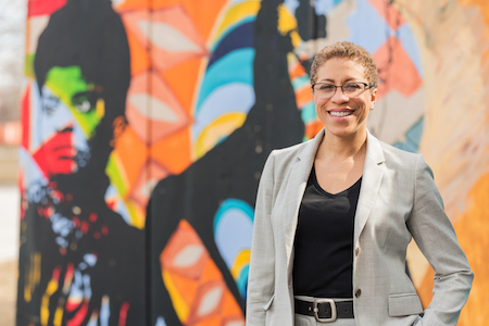 CCICS Director Andrea Evans stands in front of a colorful mural