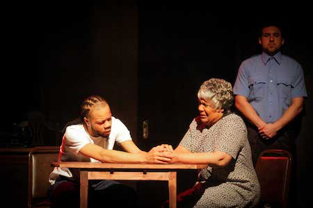 Two actors sit at a table while performing a Black Ensemble Theater play.