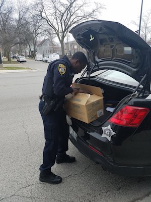 A male police officer places a cardboard box into the trunk of a police car