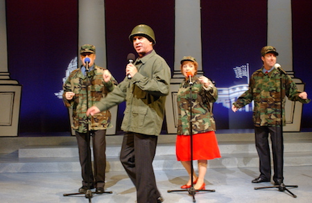 Four members of The Capitol Steps perform on stage.