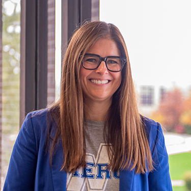 Sarah Cordell smiles into the camera while wearing a blue blazer and glasses.