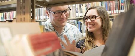 John and Marianela Crissman smile at each other while standing among library bookshelves