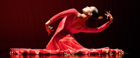 A woman dances in a red dress against a black background