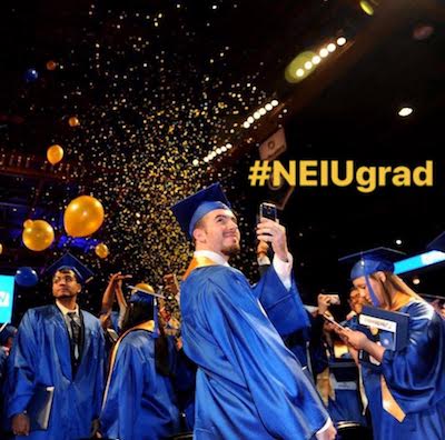 A male graduate wearing blue cap and gown takes a selfie at Commencement