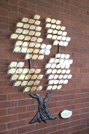 The metal memorial tree hangs on an interior brick wall