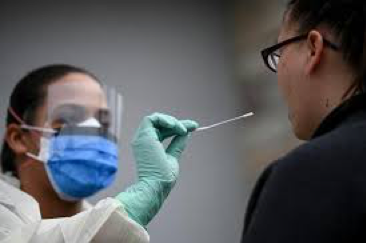 A masked and gloved health worker prepares to swab test a patient