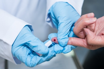 Hands wearing blue gloves hold another persons finger to take a blood sample
