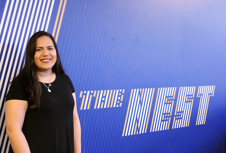 Isabel Vargas smiles while standing in front of a sign that says "The Nest."