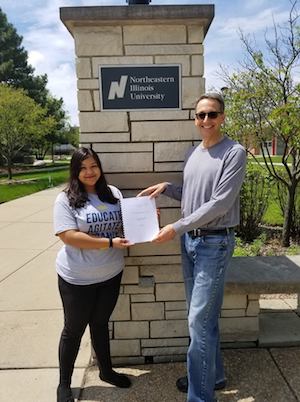 Honors graduate Lizbeth Rosas poses with Anthropology Professor and Honors Program Coordinator Jon Hageman in front of a brick entrance to the Main Campus.