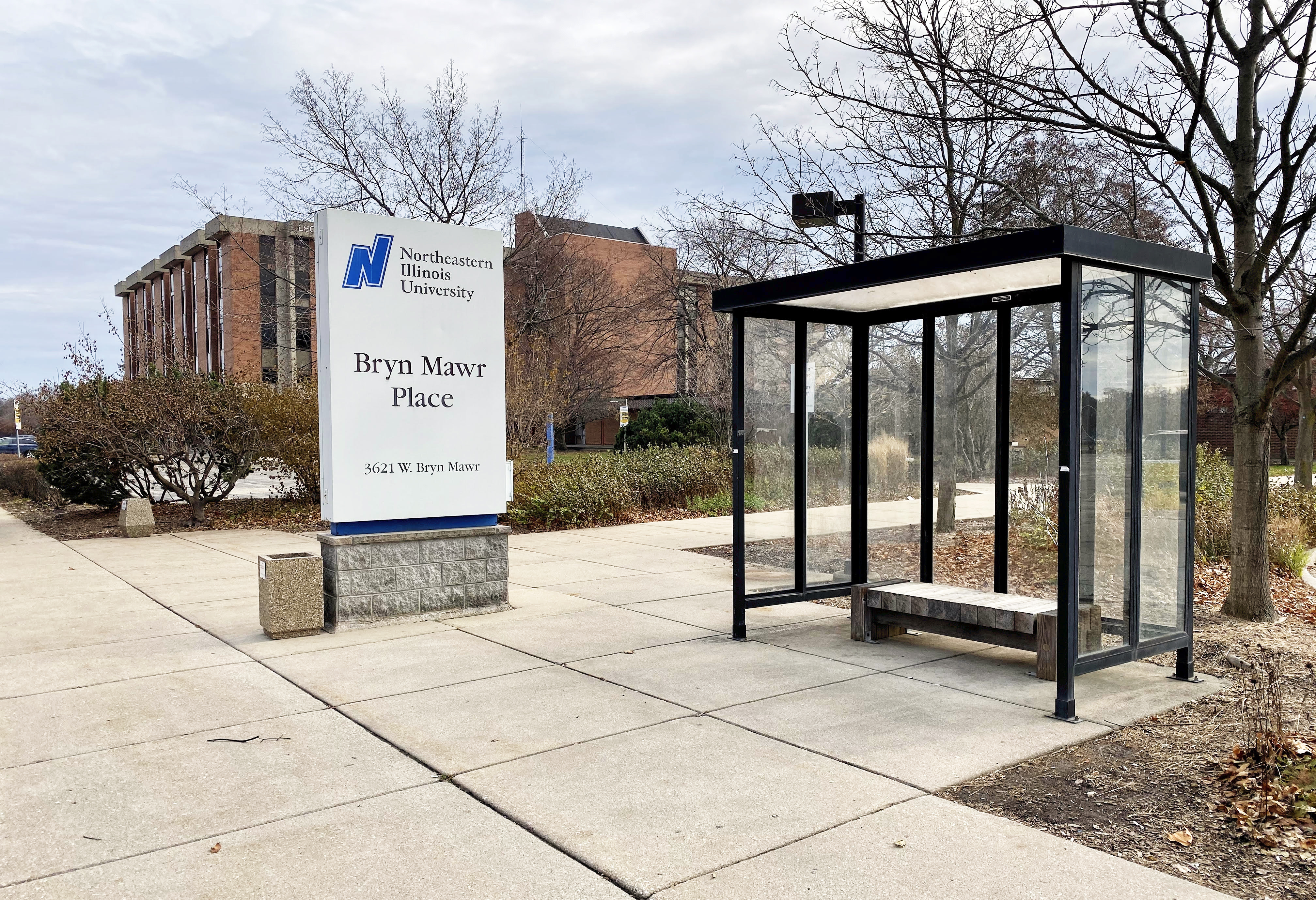 A covered bus stop next to a white street sign for Northeastern Illinois University.